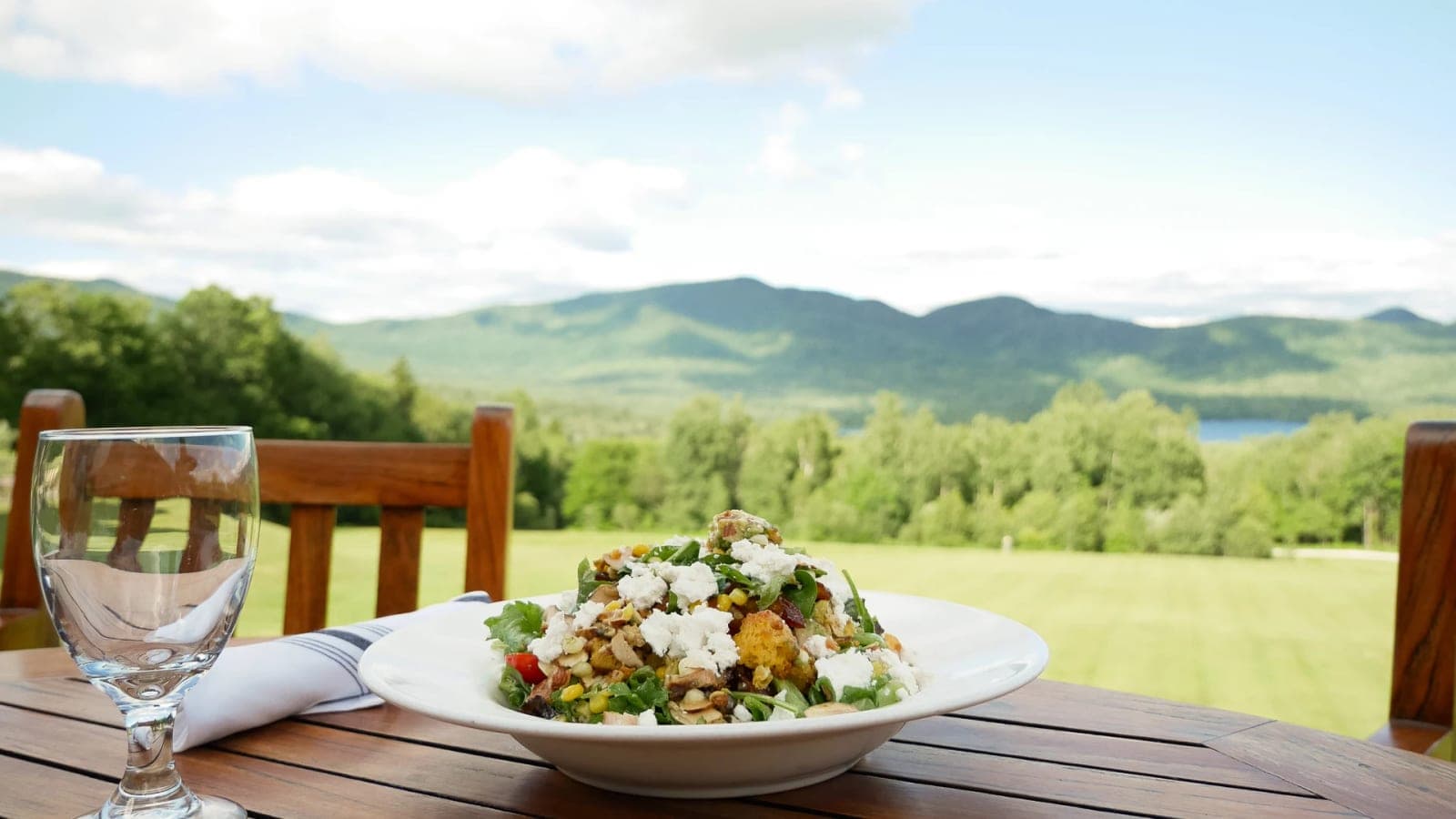 A meal on a deck table overlooking the mountains and lake.